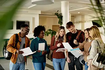 younger group of diverse people standing together looking at documents and computer screens