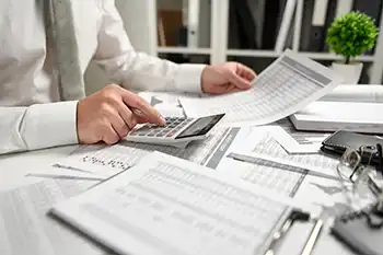 documents scattered on a desk with a pair of hands checking figures on a calculator
